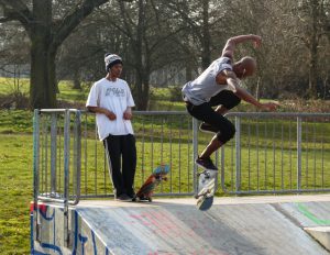 Birmingham, United Kingdom - March 14, 2014: Two skateboarders on a ramp, one performing a flip kick, the other leaning against the railings at the top watching with headphone's in his ears.